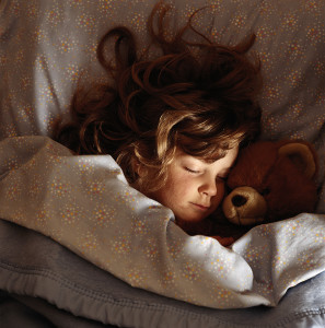 Jente som sover med en teddybjørn på armen. 