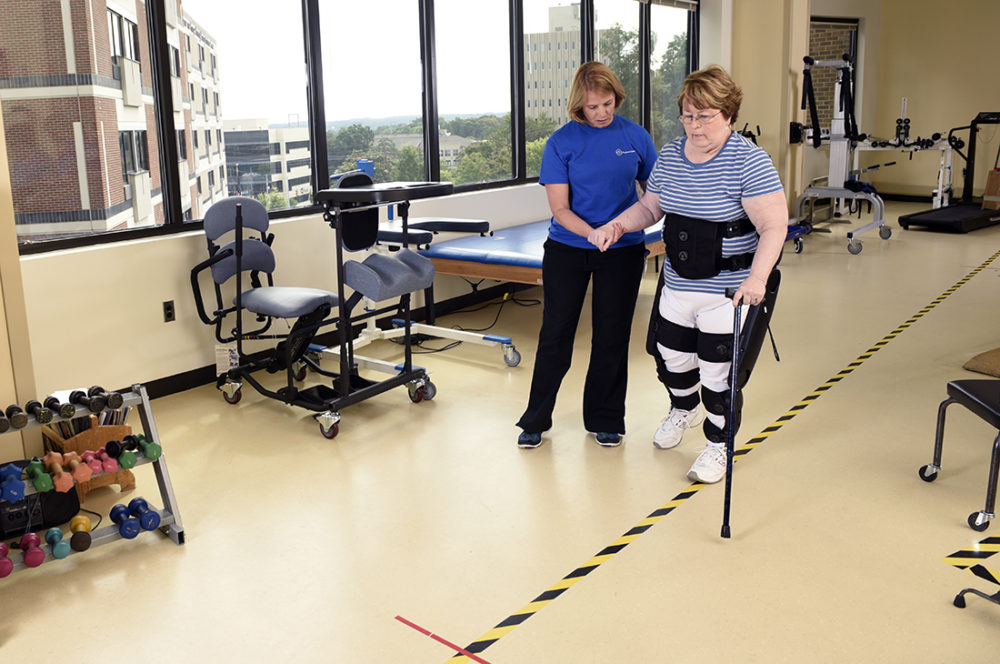A woman tries to walk assisted by another woman and an exoskeleton