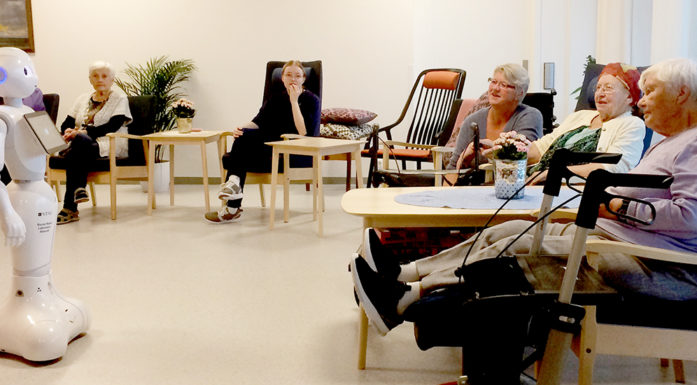 A small humanoid robot is introduced to a group of seated elderly people