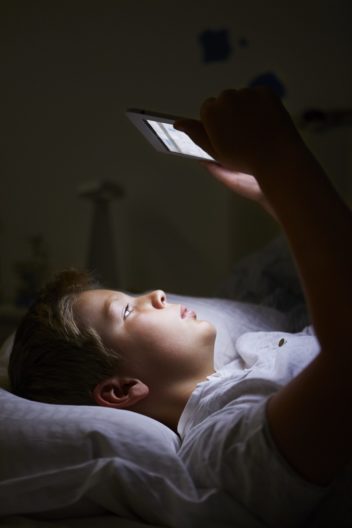 A child looking at a tablet while in bed