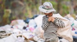 A child carrying a bag past a landfill