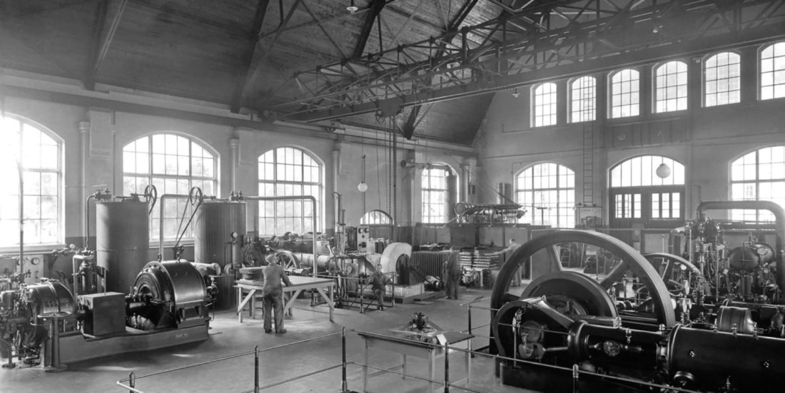 Interior from the old thermal power laboratory at the Norwegian University of Technology. The picture shows machines and equipment and people at work.