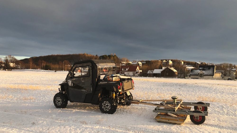 A tiny car with georadar equipment hanging of the back on a snowy field