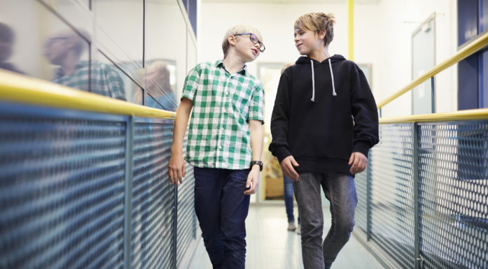 Boy talking with male friend while walking in school corridor