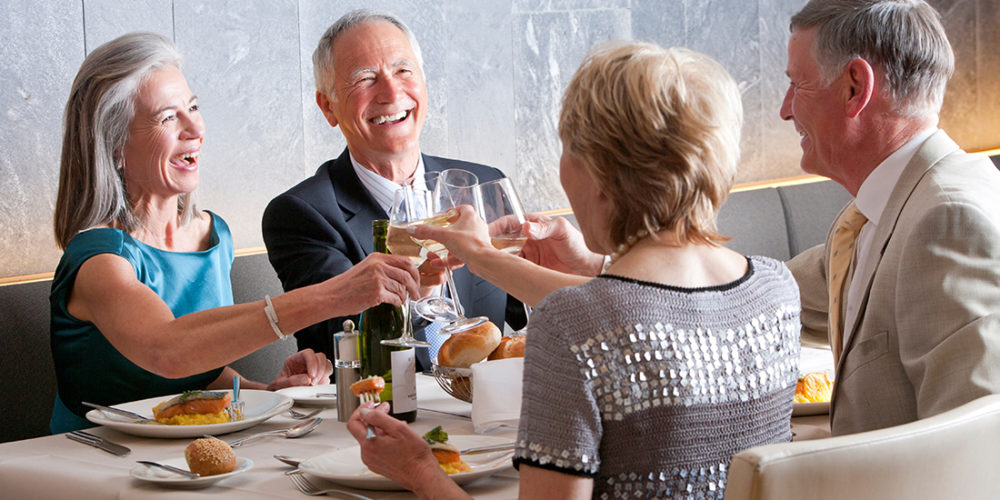 Two senior couples on a double date enjoying together while toasting the wine glasses at a restaurant table
