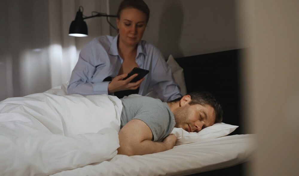 Woman checking man's phone while he sleeps