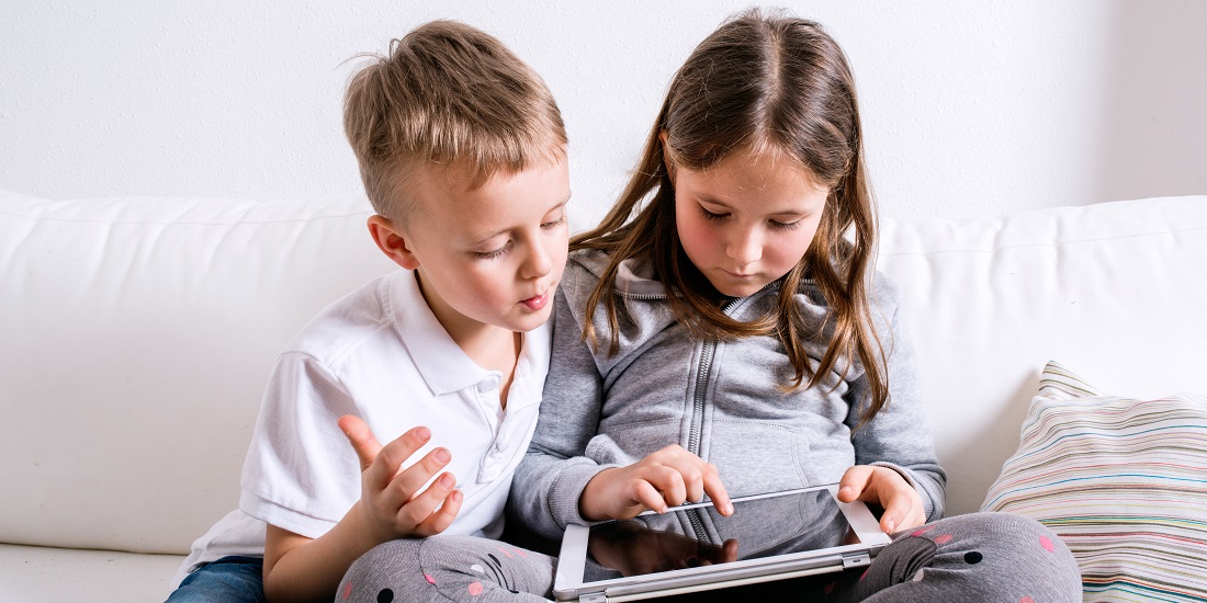 Children at home sitting on sofa, playing with tablet