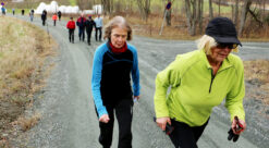 Two elderly women runners ahead of a group of walkers on dirt path. Photo.