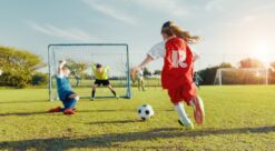 Children playing football with a girl about to kick a ball.