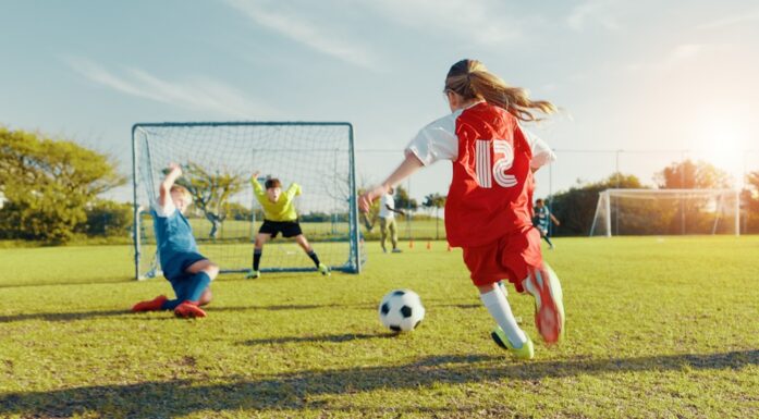 Children playing football with a girl about to kick a ball.