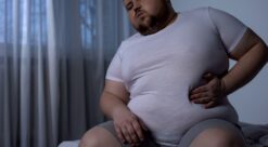 Heavyset man in t-shirt scratching belly. Photo.