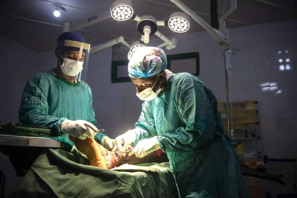 Two Sierra Leone surgeons work on an ulcerated ankle. Photo.