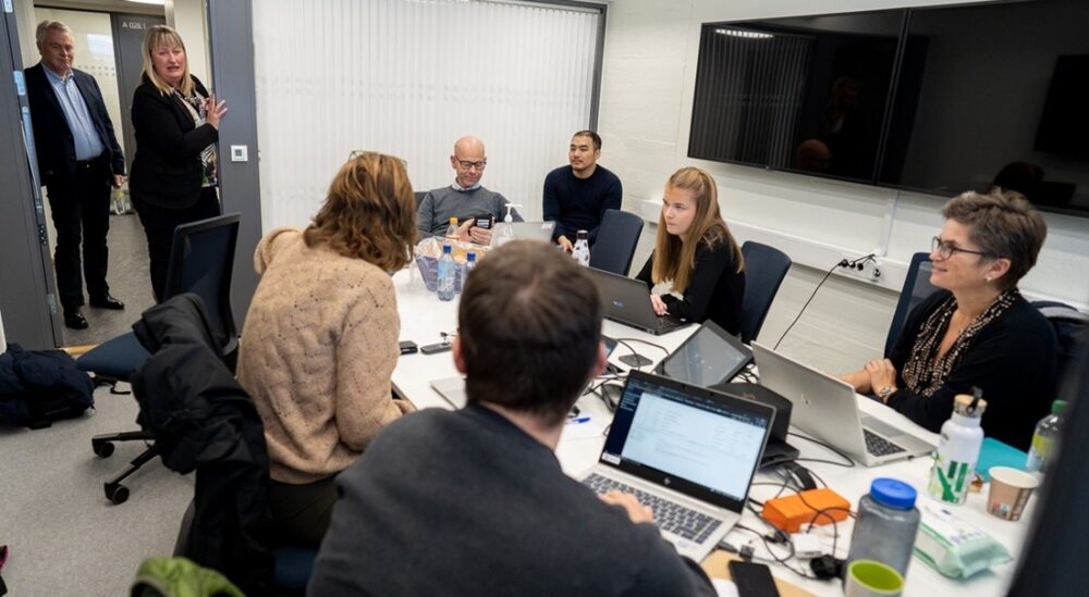 Six people sitting around a table in a small room during a cyber security exercise. Photo.