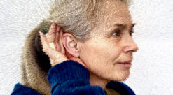 Woman with her hand cupping her ear to improve hearing. Photo illustration.