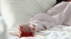Hand of person in bed holding an alcoholic drink.