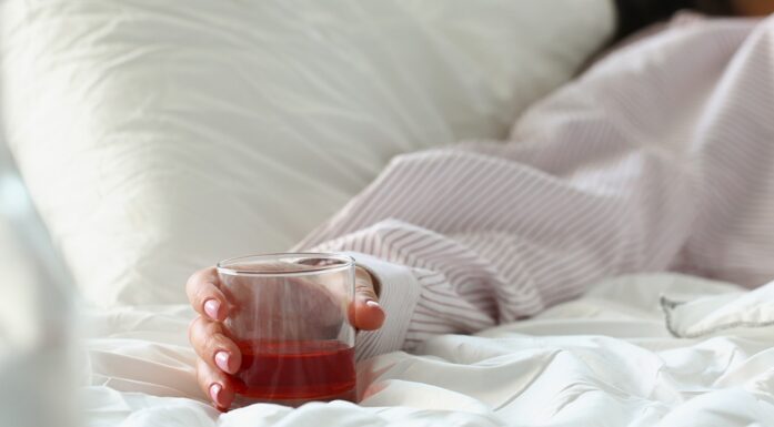 Hand of person in bed holding an alcoholic drink.