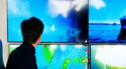 Man sitting in front of big computer screens with ocean images. Photo.