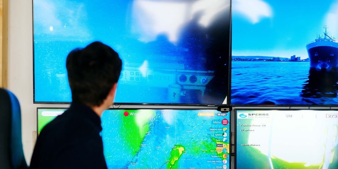 Man sitting in front of big computer screens with ocean images. Photo.