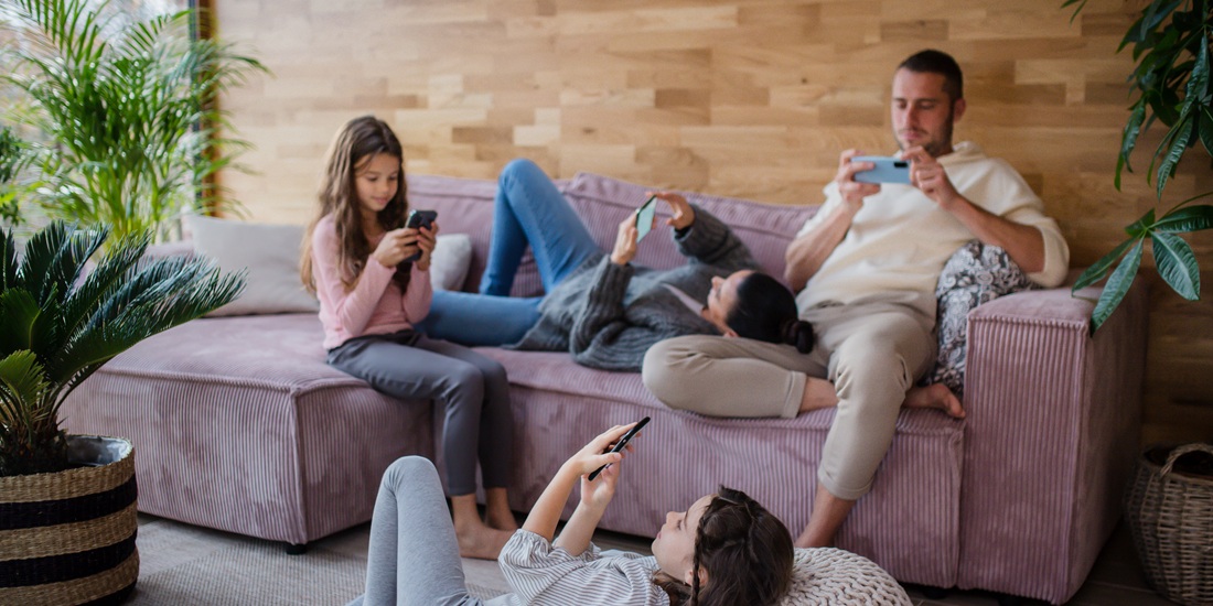 A family with two little daughters, everyone is using mobile phone in the living room.